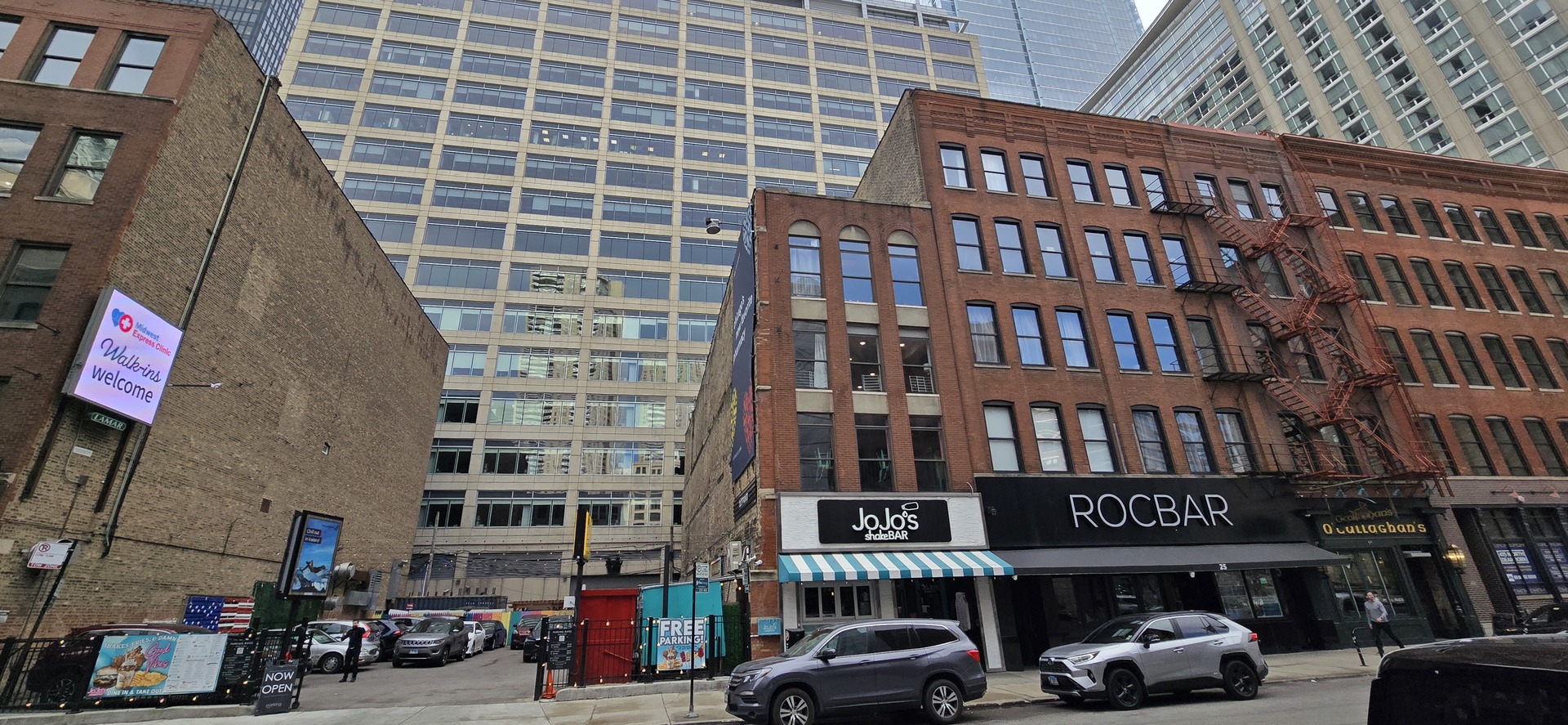 a front view of a building with lot of cars and trees