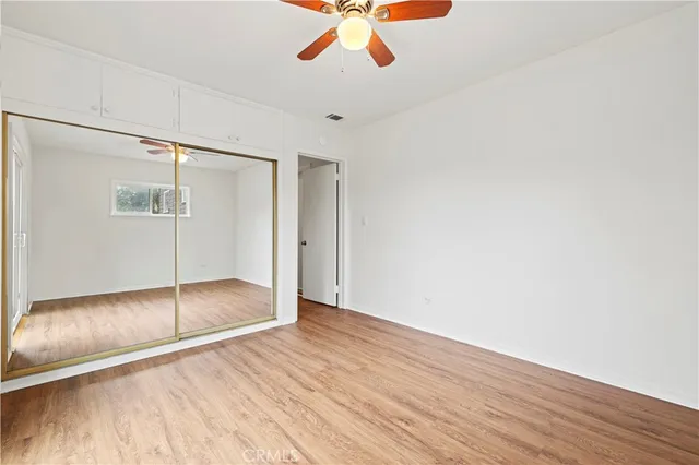 a view of an empty room with wooden floor and a ceiling fan