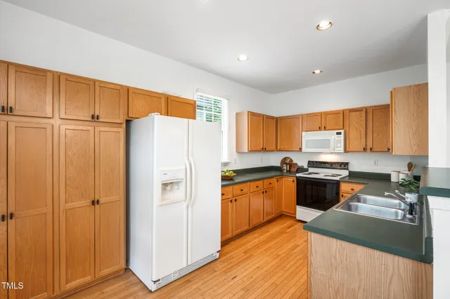 a kitchen with stainless steel appliances granite countertop a refrigerator a sink dishwasher a stove and white countertops with wooden floor