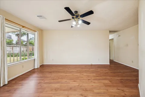 an empty room with wooden floor fan and windows