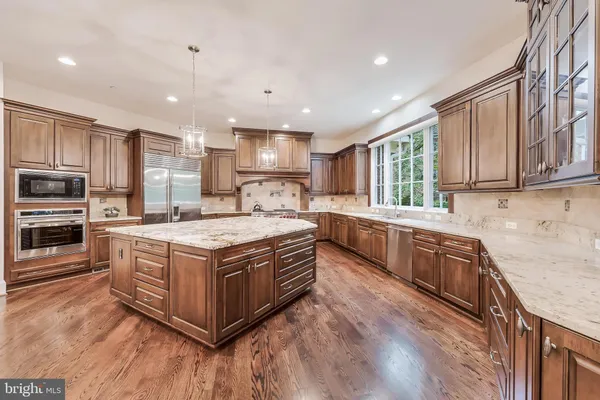 a large kitchen with stainless steel appliances granite countertop a stove a sink dishwasher a refrigerator white cabinets and wooden floor