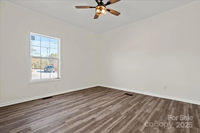 an empty room with wooden floor chandelier fan and windows