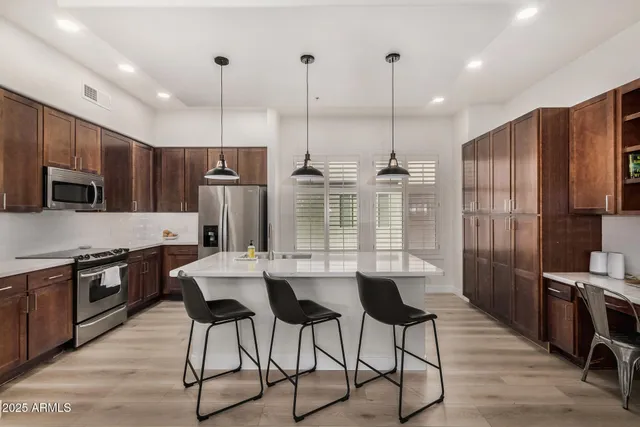 a kitchen with stainless steel appliances kitchen island granite countertop a refrigerator a stove a sink a dining table and chairs with wooden floor