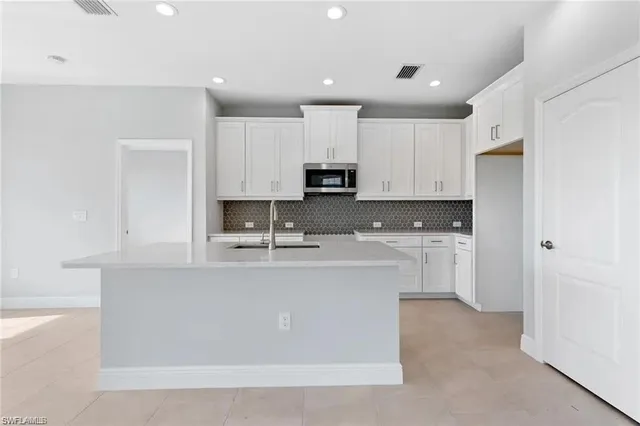 a large kitchen with stainless steel appliances granite countertop a stove a sink a refrigerator and white cabinets with wooden floor