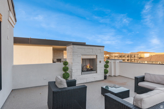 5367 Cyan Lane St. George, UT 84790 - Photo 35 of 49 Rooftop patio featuring a stone-clad fireplace with a dark metal frame, a flat-top roofline, white stucco walls, and a textured gray flooring surface