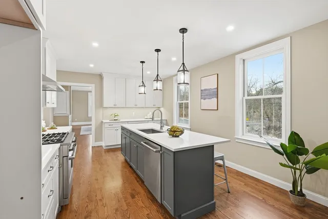 a kitchen with stainless steel appliances a stove a sink a refrigerator a center island and a wooden floor