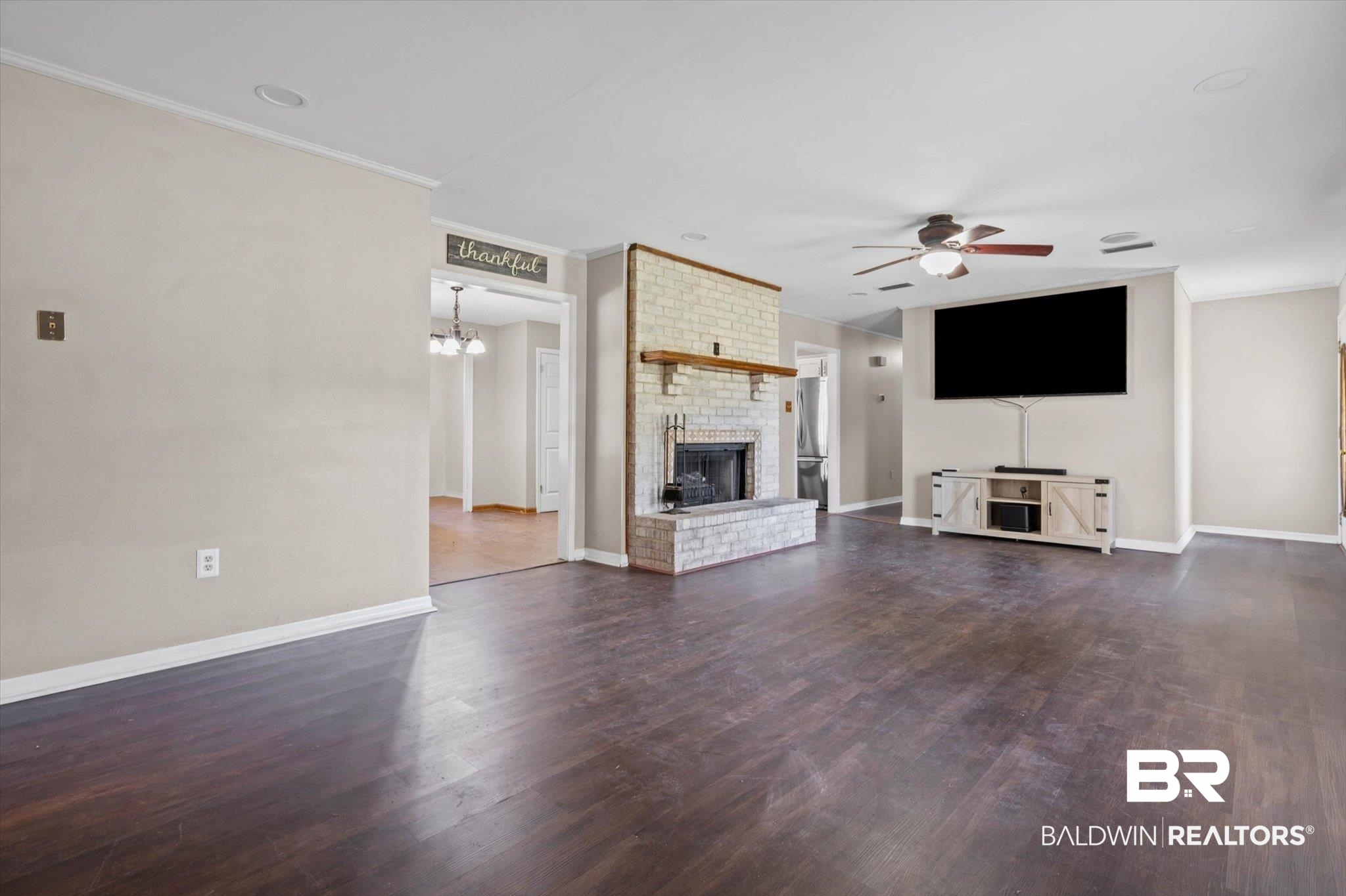 180 Creax Road Axis, AL 36505 - Photo 3 of 35 Unfurnished living room with crown molding, dark wood-style floors, a ceiling fan, a fireplace, and a chandelier