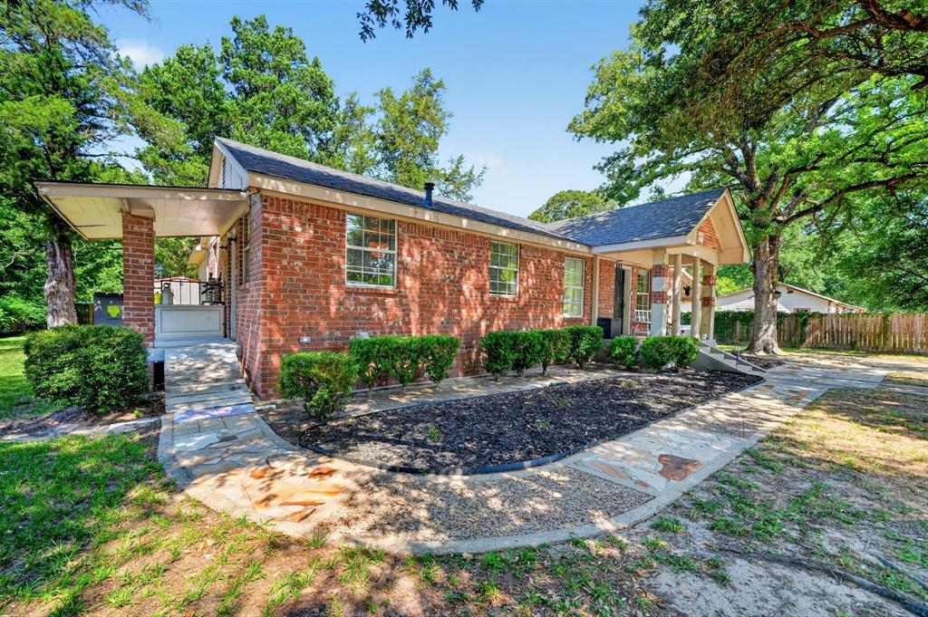 810 Edna Street Athens, TX 75751 - Photo 3 of 28 Brick exterior home featuring a covered front porch, an additional covered entry with ramp access, a flagstone walkway, mature trees, and landscaping with shrubbery