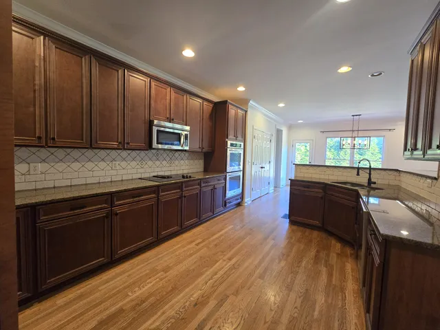 a kitchen with stainless steel appliances granite countertop wooden cabinets a stove top oven with wooden floor