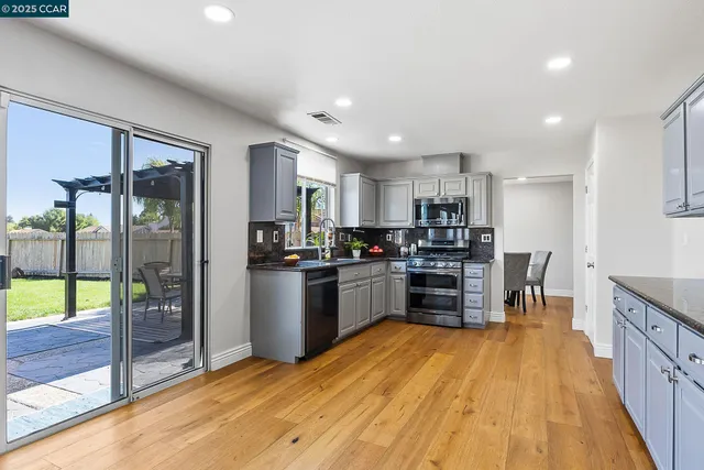 a kitchen with stainless steel appliances kitchen island granite countertop a refrigerator a stove top oven and a sink with wooden floor