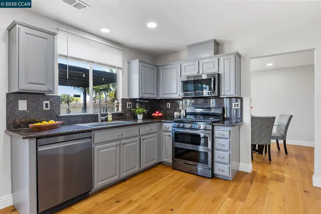 a kitchen with stainless steel appliances granite countertop a stove top oven a sink dishwasher and white cabinets with wooden floor