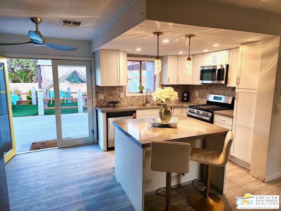 a kitchen with stainless steel appliances granite countertop a stove a refrigerator a sink a dining table and chairs with wooden floor