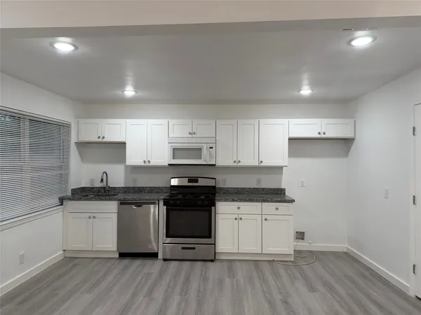 a kitchen with stainless steel appliances granite countertop a stove a sink and white cabinets