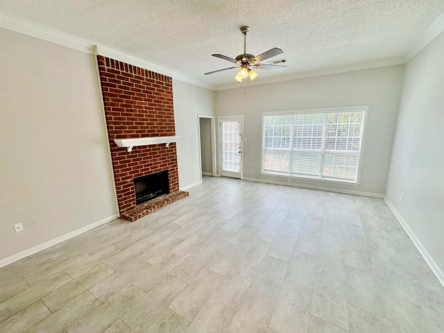779 North Sanga Road Memphis, TN 38018 - Photo 5 of 12 Unfurnished living room featuring a textured ceiling, crown molding, ceiling fan, and a brick fireplace