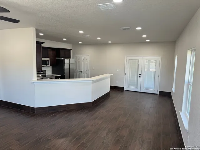 an empty room with wooden floor and way to kitchen