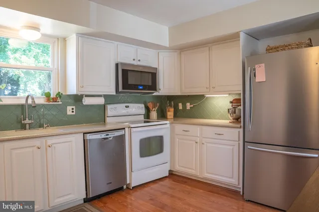 a kitchen with white cabinets white stainless steel appliances and wooden floors