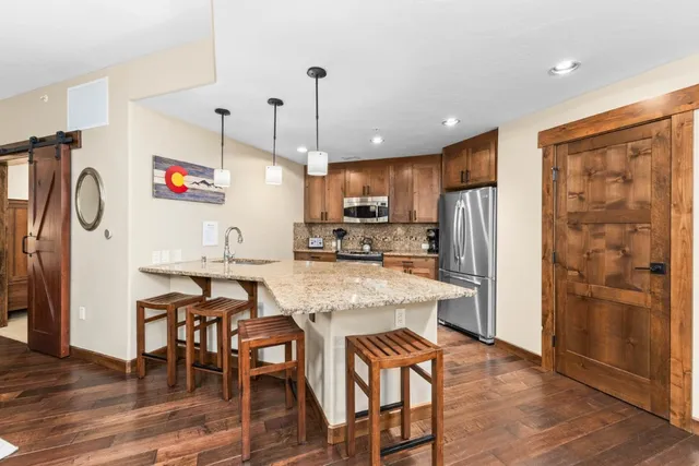 a kitchen with stainless steel appliances granite countertop a refrigerator a oven a sink a dining table and chairs with wooden floor