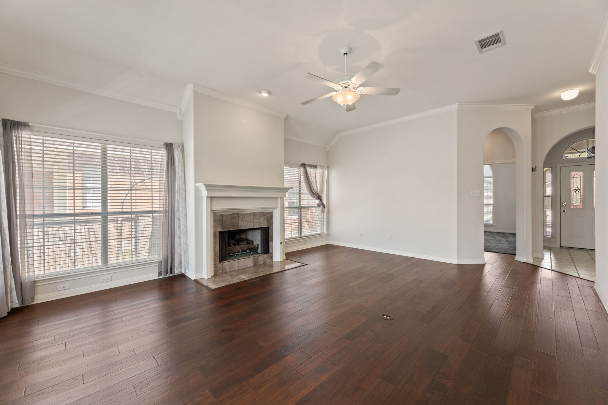 109 Riverview Drive Georgetown, TX 78628 - Photo 11 of 35 Unfurnished living room featuring ceiling fan, arched walkways, dark wood-style floors, ornamental molding, and a high end fireplace
