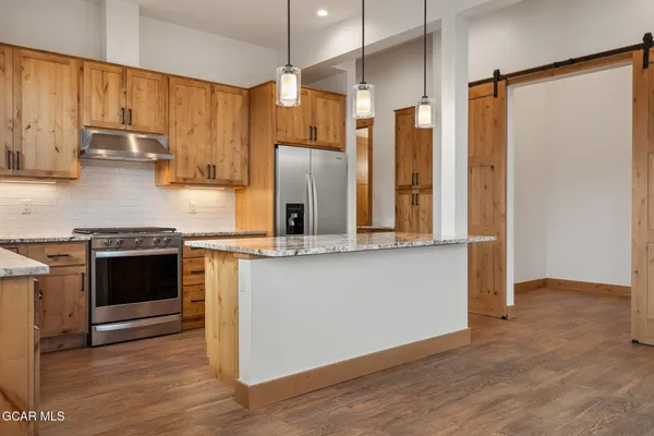 a kitchen with stainless steel appliances granite countertop a refrigerator a stove and a sink with wooden floor