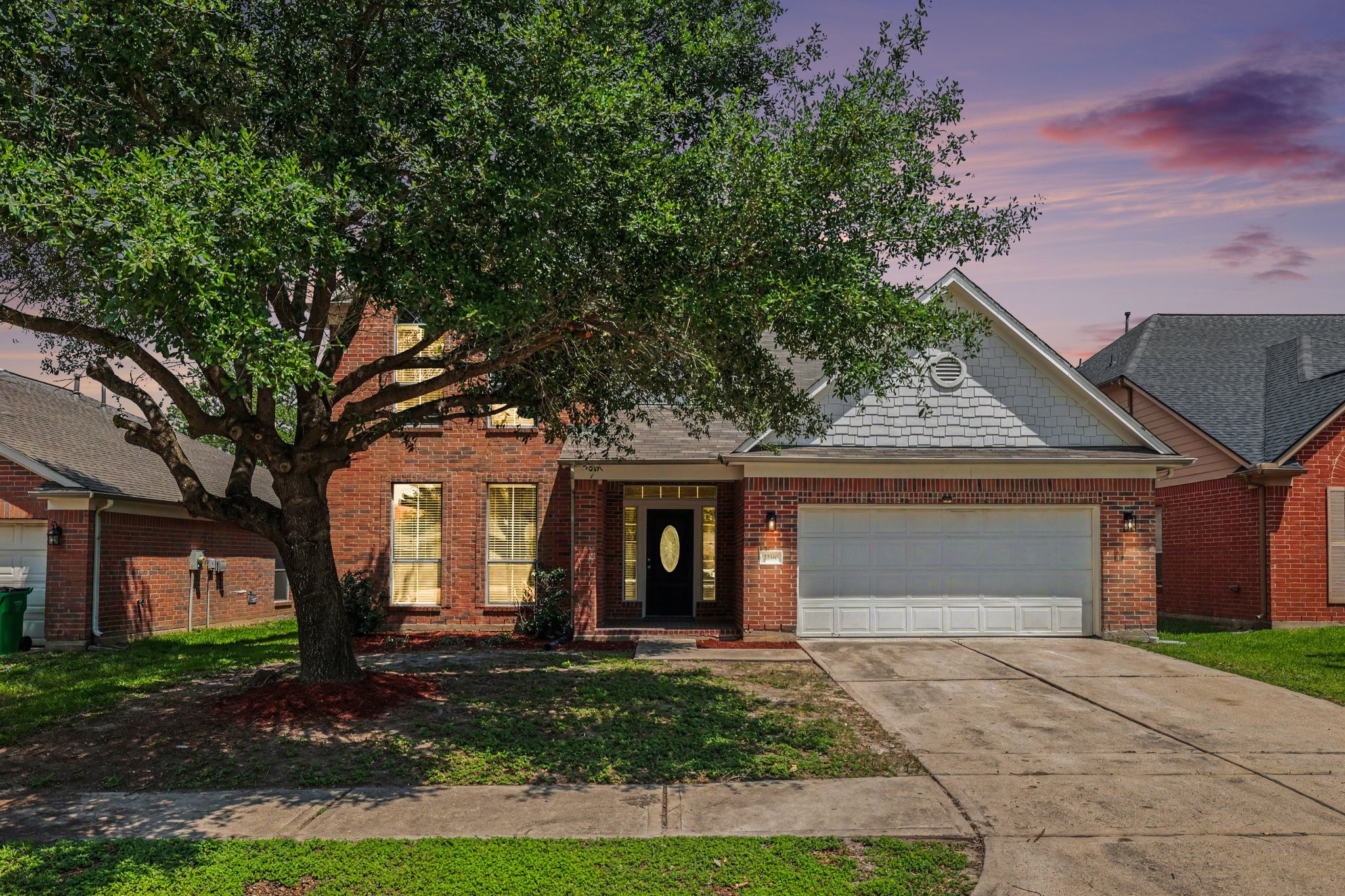 This is a charming brick home with a two-car garage and double wide driveway. It features a well-maintained front yard with a mature tree, providing shade and curb appeal.
