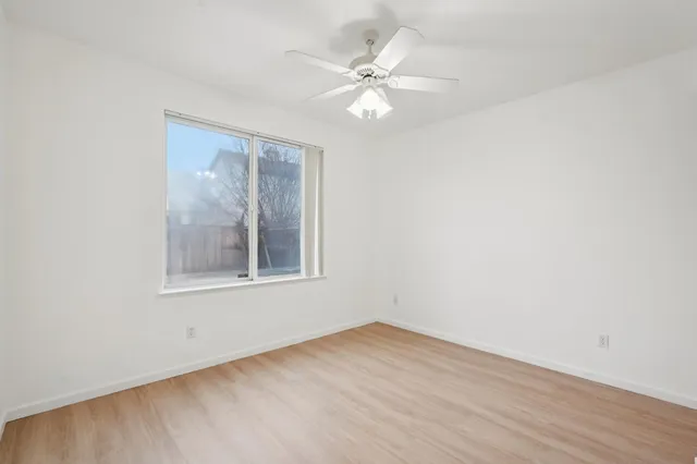a view of an empty room with wooden floor and a ceiling fan
