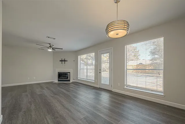an empty room with wooden floor chandelier fan and windows