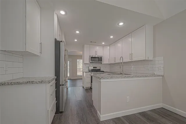 a kitchen with stainless steel appliances granite countertop a refrigerator a sink dishwasher a stove and white cabinets with wooden floor