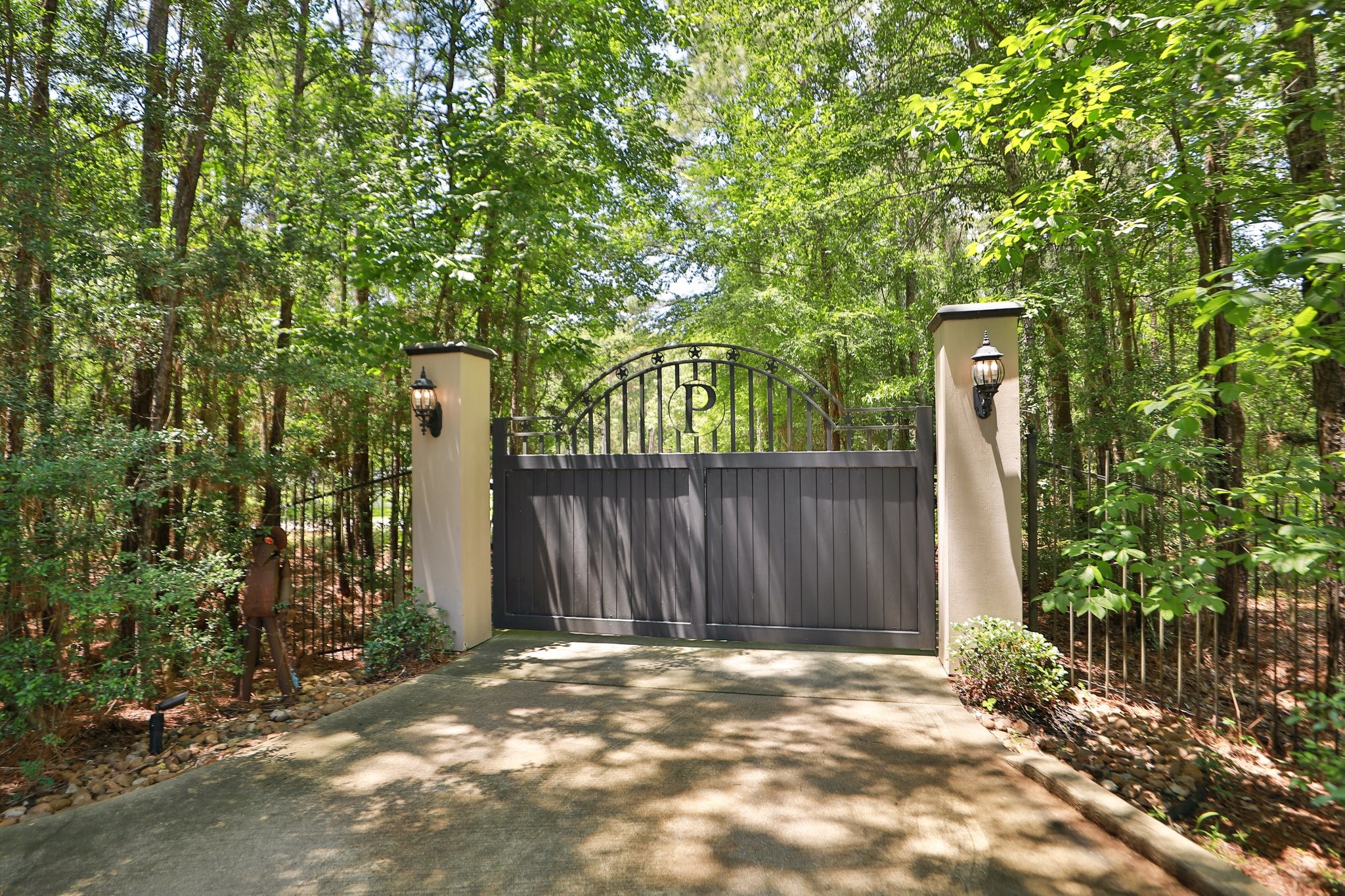 7514 Saddle Blanket Drive Waller, TX 77484 - Photo 3 of 50 This photo shows a gated driveway entrance surrounded by tall trees, with elegant pillars featuring decorative lanterns. The paved path offers privacy and a welcoming approach to the property.