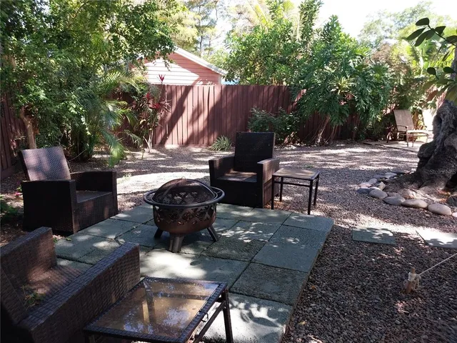 a view of a backyard with table and chairs potted plants and a large tree