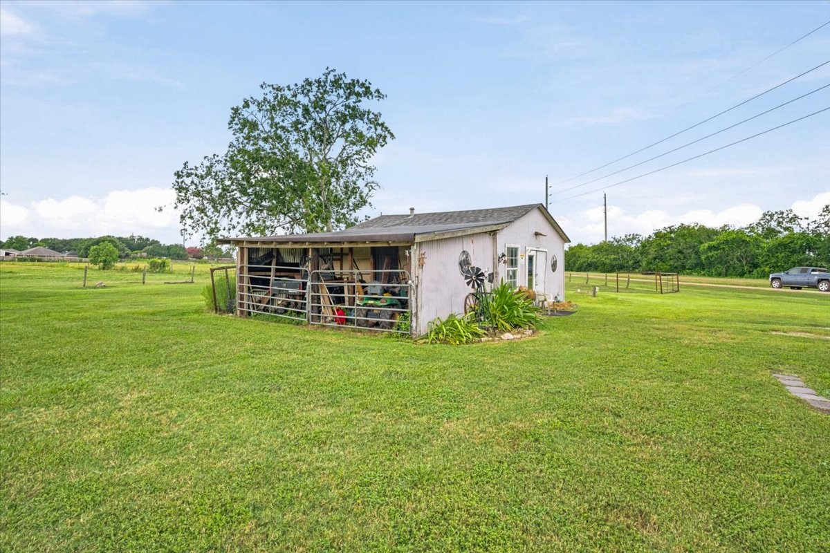 765 Norcross Road Wallis, TX 77485 - Photo 31 of 42 A charming, small white shed sits on a spacious, well-maintained grassy lot. It features rustic decor and is surrounded by open land, offering a peaceful, rural setting ideal for those seeking tranquility and space.