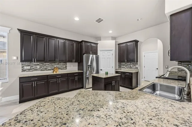 a kitchen with stainless steel appliances kitchen island granite countertop a sink stove refrigerator and cabinets