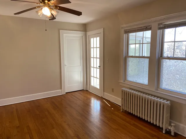 an empty room with wooden floor chandelier fan and windows