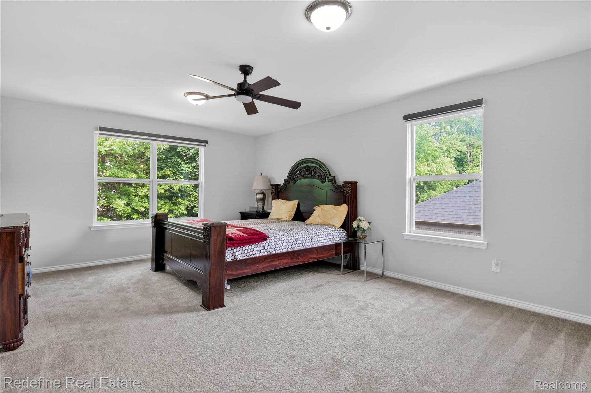 2976 Andlaur Drive Rochester, MI 48307 - Photo 31 of 60 Spacious bedroom with light gray walls, plush carpeting, two large windows with roller shades, a ceiling fan with integrated lighting, and a flush-mount ceiling light fixture