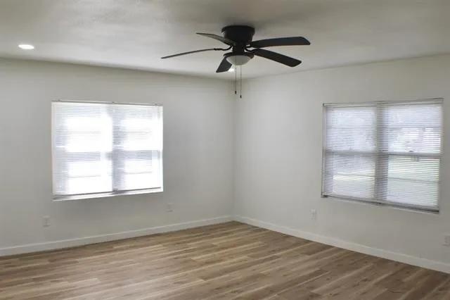 an empty room with wooden floor fan and windows