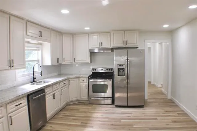 a kitchen with stainless steel appliances granite countertop a refrigerator a sink and white cabinets