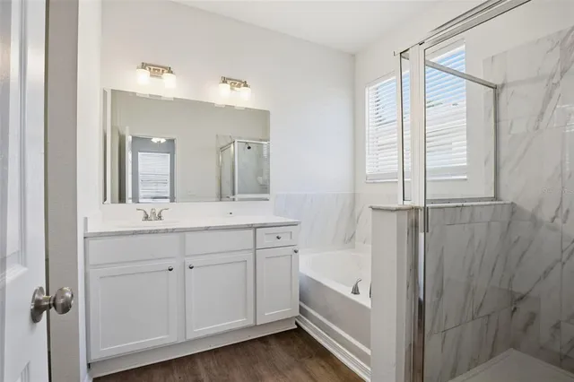 a bathroom with a double vanity sink a mirror a bathtub and next to a window