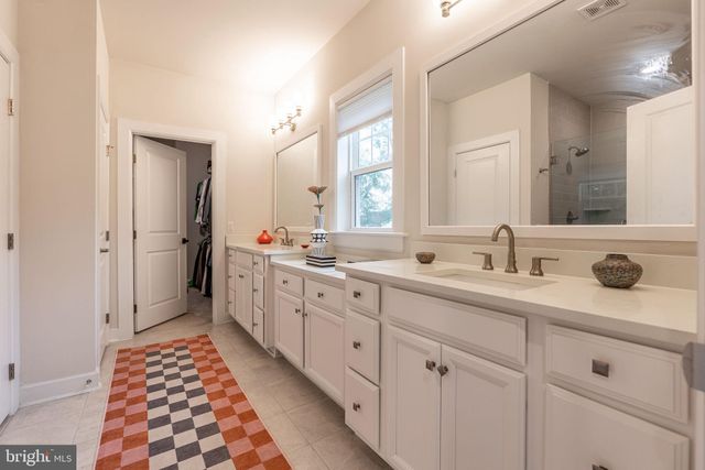 a spacious bathroom with double sink a two mirror a window and a shower