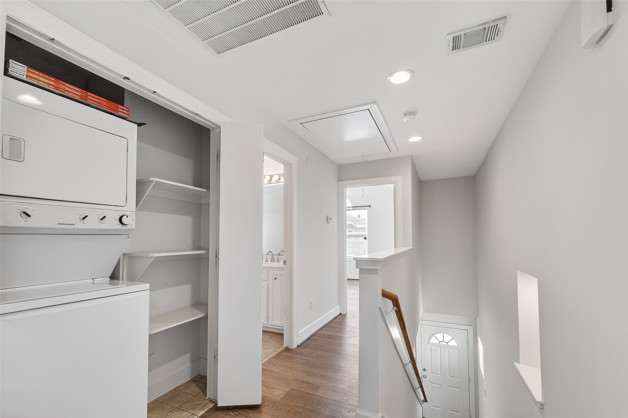 5951 S Loop East, Unit 47 Houston, TX 77033 - Photo 23 of 37 The bright hallway with hardwood flooring, featuring a convenient in-wall stacked washer and dryer, open shelving, recessed lighting, and access to an adjacent room and staircase.