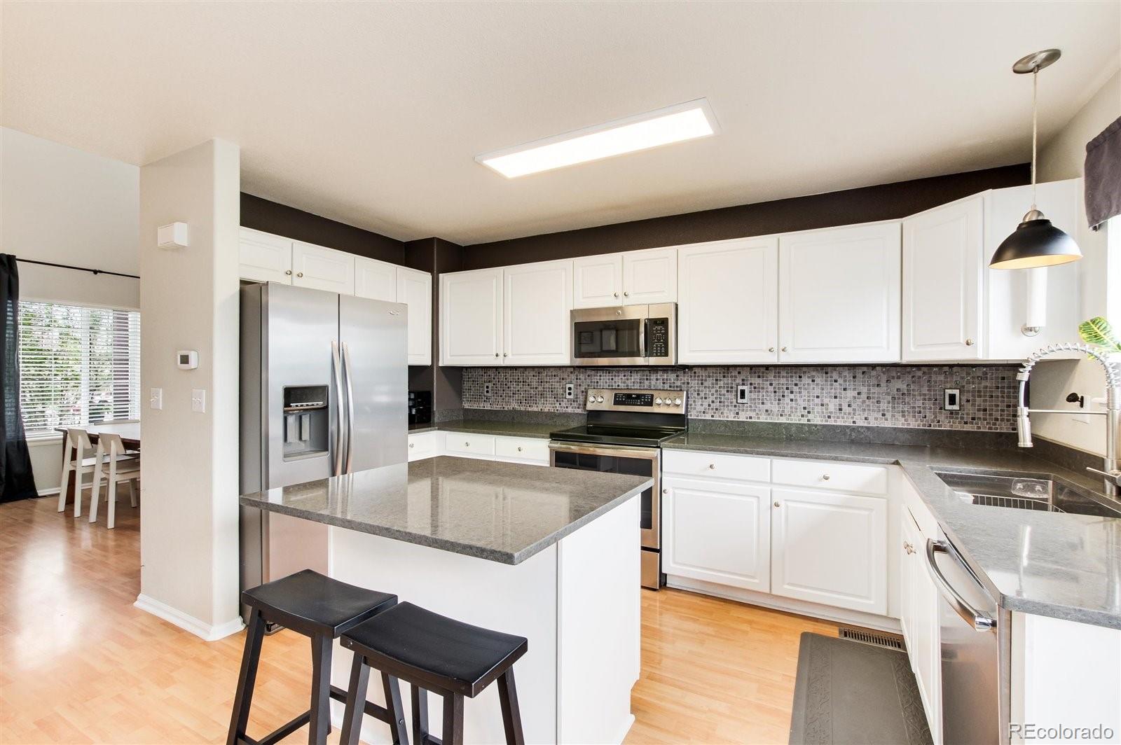 9701 Moss Rose Circle Highlands Ranch, CO 80129 - Photo 13 of 40 a kitchen with stainless steel appliances granite countertop a stove a sink a microwave a refrigerator white cabinets and wooden floor