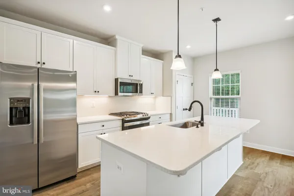 a kitchen with stainless steel appliances kitchen island a sink a refrigerator a counter space and wooden floor