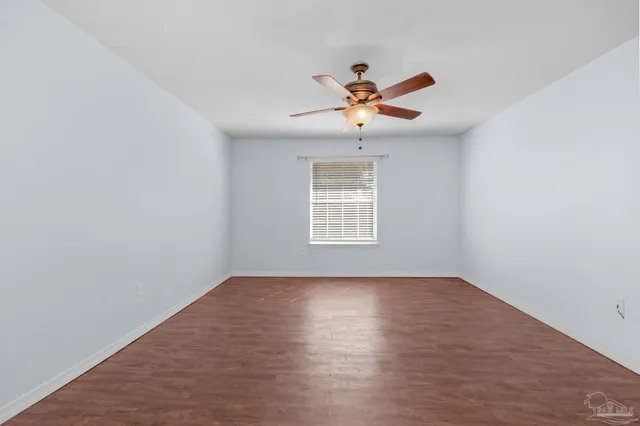 an empty room with wooden floor fan and windows