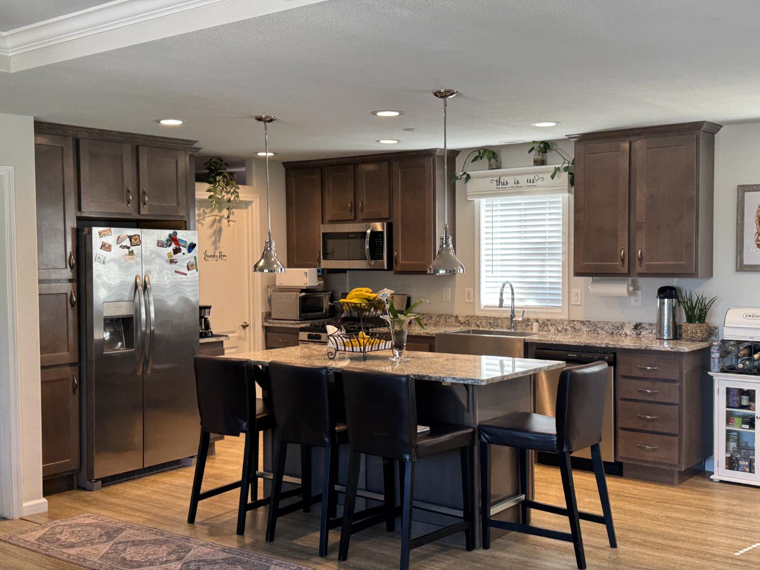 12379 Clay Station Road Herald, CA 95638 - Photo 6 of 14 Kitchen featuring a central island with bar seating, wood-finish flooring, dark wood cabinetry, light-colored countertops, and stainless steel appliances