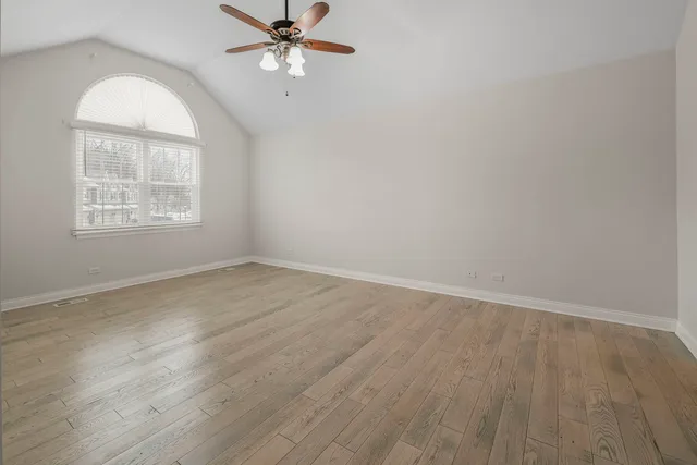 an empty room with wooden floor chandelier fan and windows