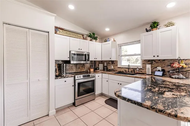 a kitchen with granite countertop white cabinets stainless steel appliances a sink and a window