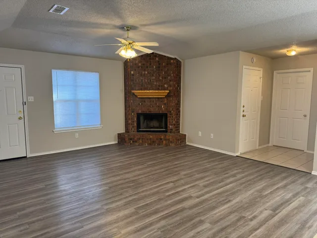 a view of an empty room with wooden floor fireplace and a window
