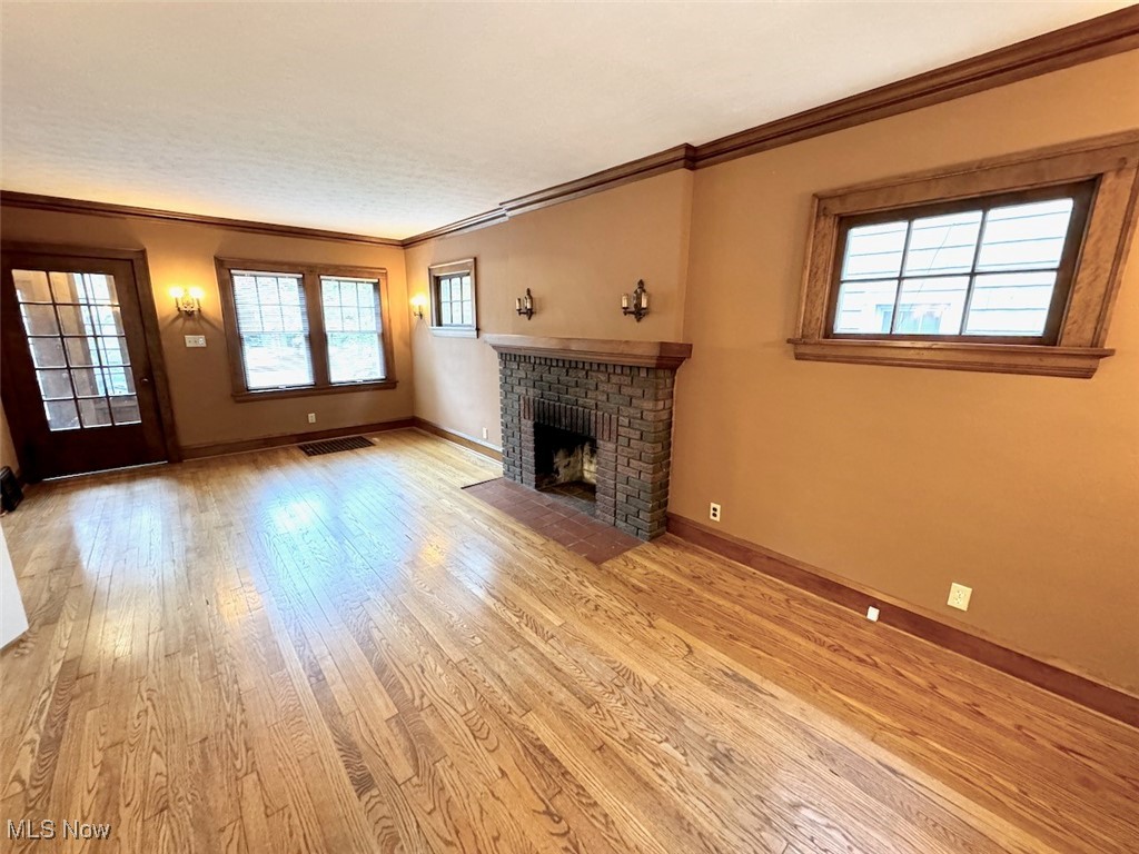 1011 Rushleigh Road Cleveland, OH 44121 - Photo 3 of 27 Unfurnished living room featuring a fireplace, a wealth of natural light, crown molding, and light hardwood flooring