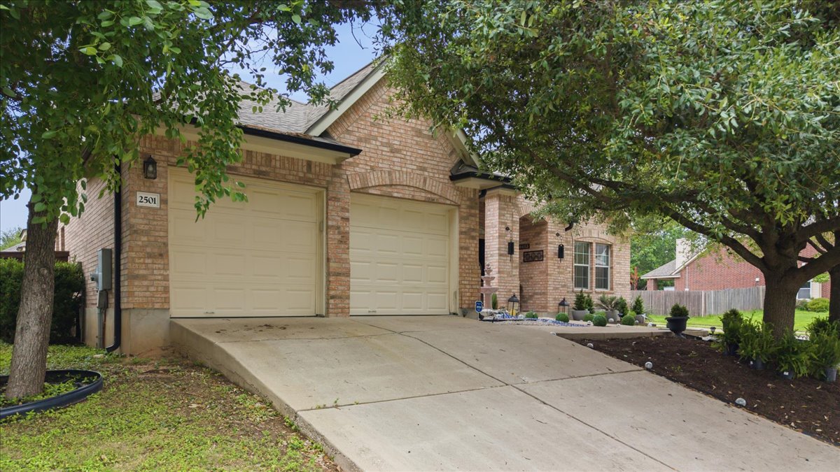 2501 Aspen Meadow Road Leander, TX 78641 - Photo 4 of 30 Brick-clad exterior featuring a two-car garage, concrete driveway, covered porch entry, and established landscaping beds