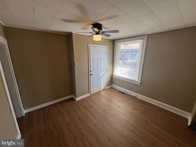 an empty room with wooden floor chandelier fan and windows