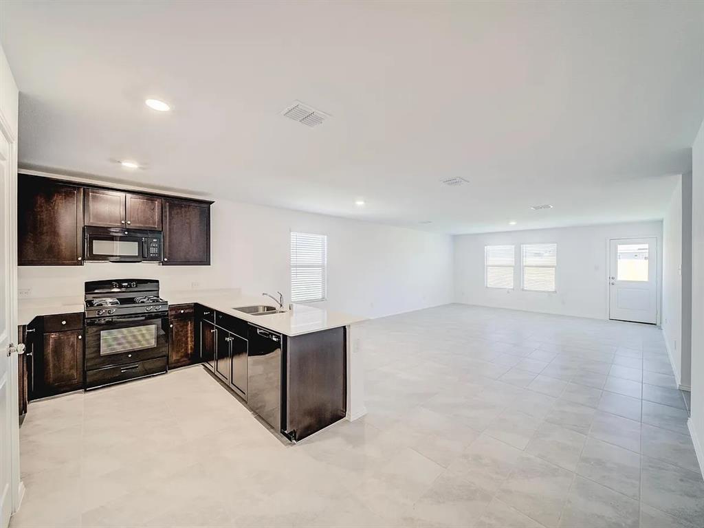 352 Sun Bluff Road Fort Worth, TX 76052 - Photo 8 of 33 Open-concept living area featuring a kitchen with dark wood-finish cabinetry, light countertops, and dark appliances