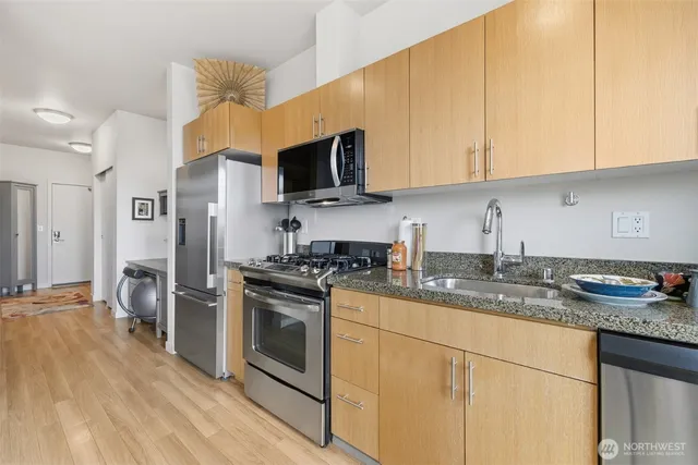 a kitchen with stainless steel appliances granite countertop a stove a sink dishwasher and a refrigerator with wooden floor